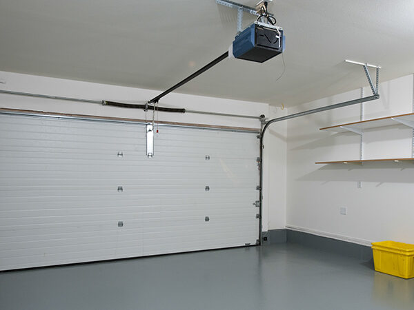 Interior view of a modern garage featuring a closed white garage door, overhead garage door opener, and organized shelving with a yellow storage bin, highlighting residential garage services by Prime Secured Garageus.