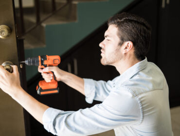 Profile view of an attractive handyman using a power drill to fix a door knob in a house