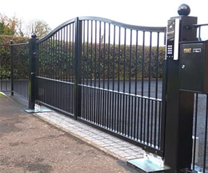 Electric gate with modern design, featuring vertical bars and a keypad for access control, set in a landscaped environment, relevant to Prime Secured Garage Door & Gate's installation and repair services.
