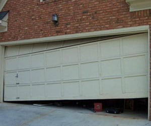 Garage door off track with visible damage, illustrating a need for repair services from Prime Secured Garage Door & Gate in Fort Worth.